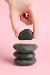 Photo of Woman making stack of stones on light pink background, closeup. Harmony and life balance