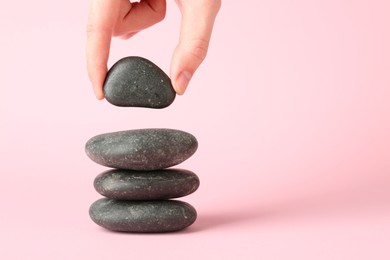 Photo of Woman making stack of stones on light pink background, closeup with space for text. Harmony and life balance