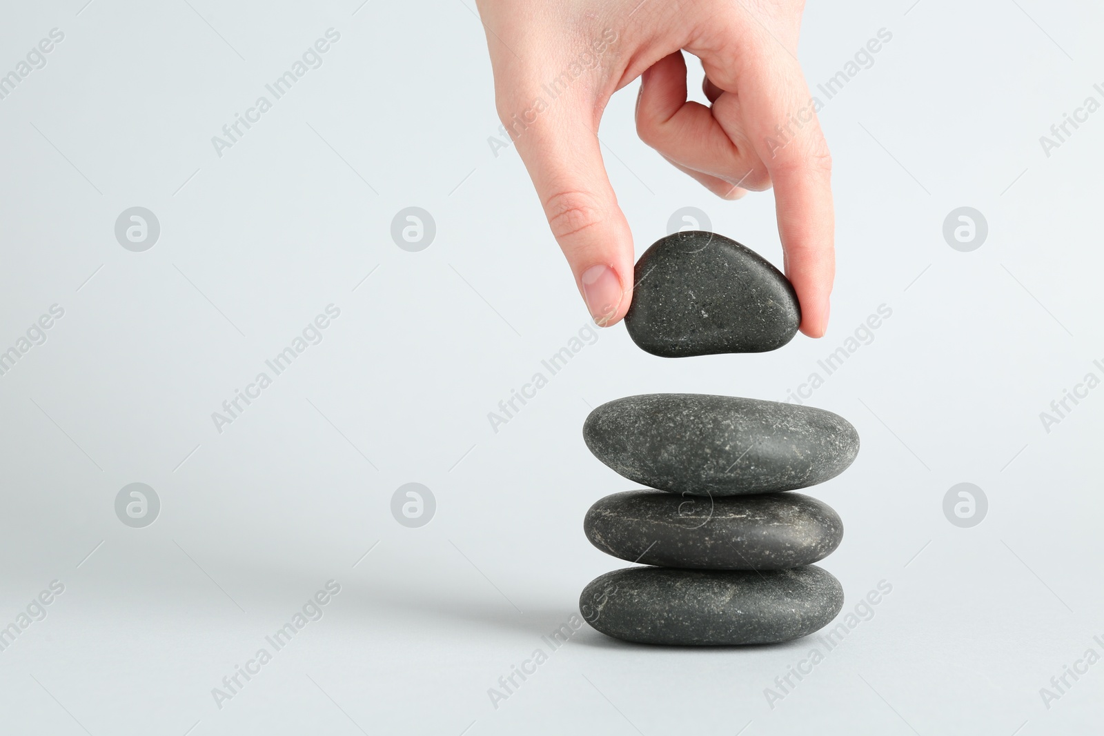 Photo of Woman making stack of stones on light background, closeup with space for text. Harmony and life balance