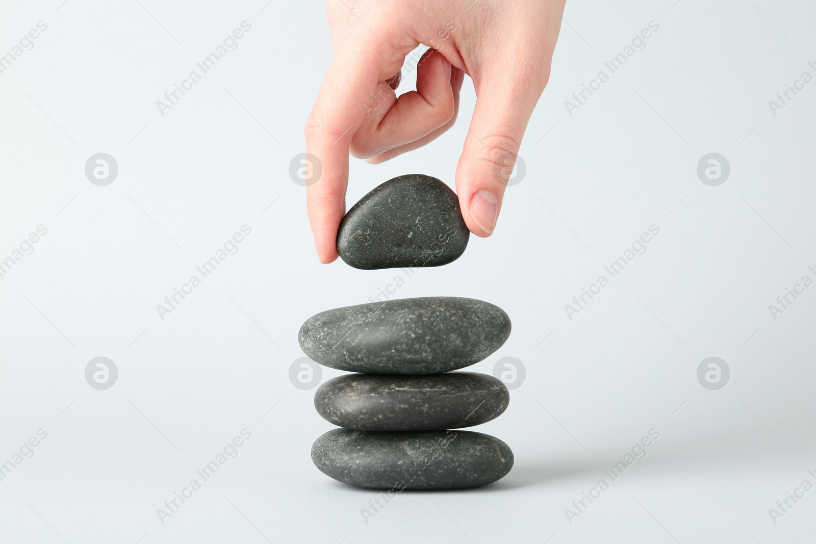 Photo of Woman making stack of stones on light background, closeup. Harmony and life balance