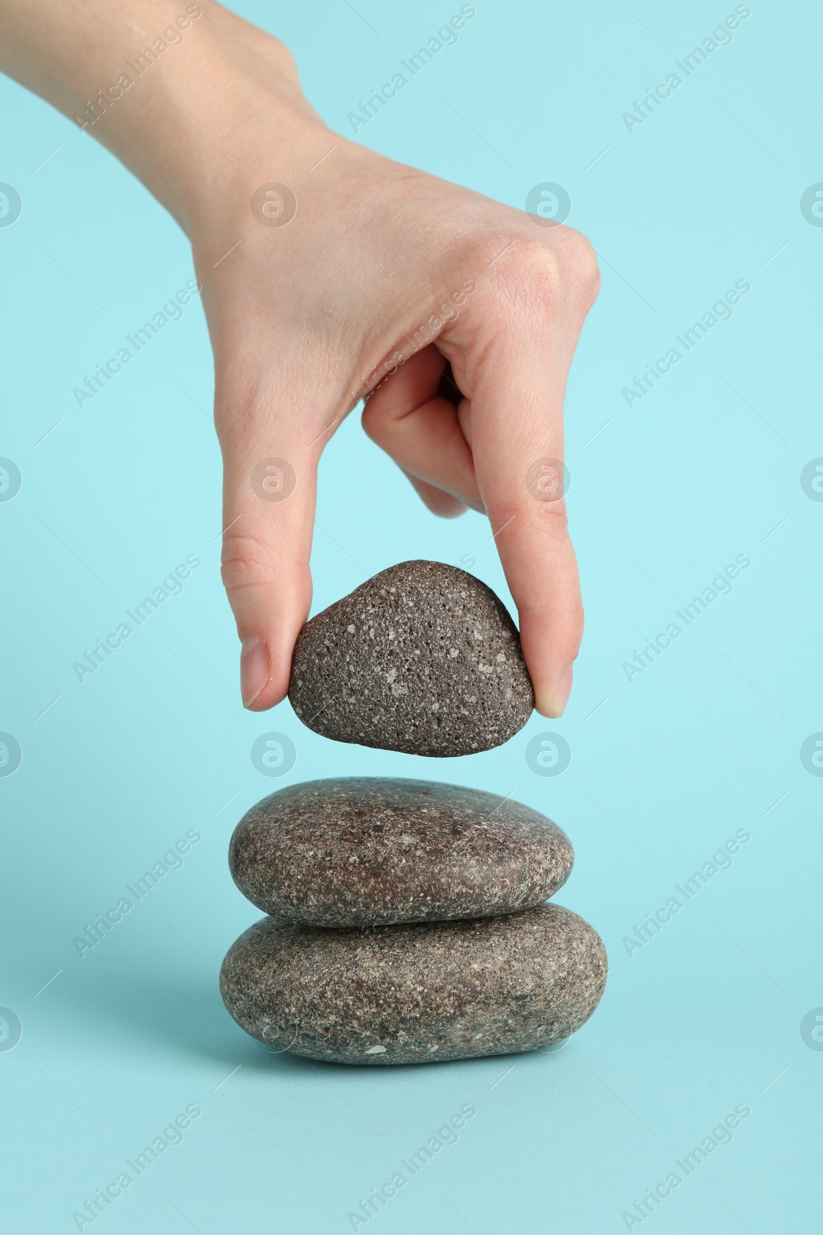 Photo of Woman making stack of stones on light blue background, closeup. Harmony and life balance