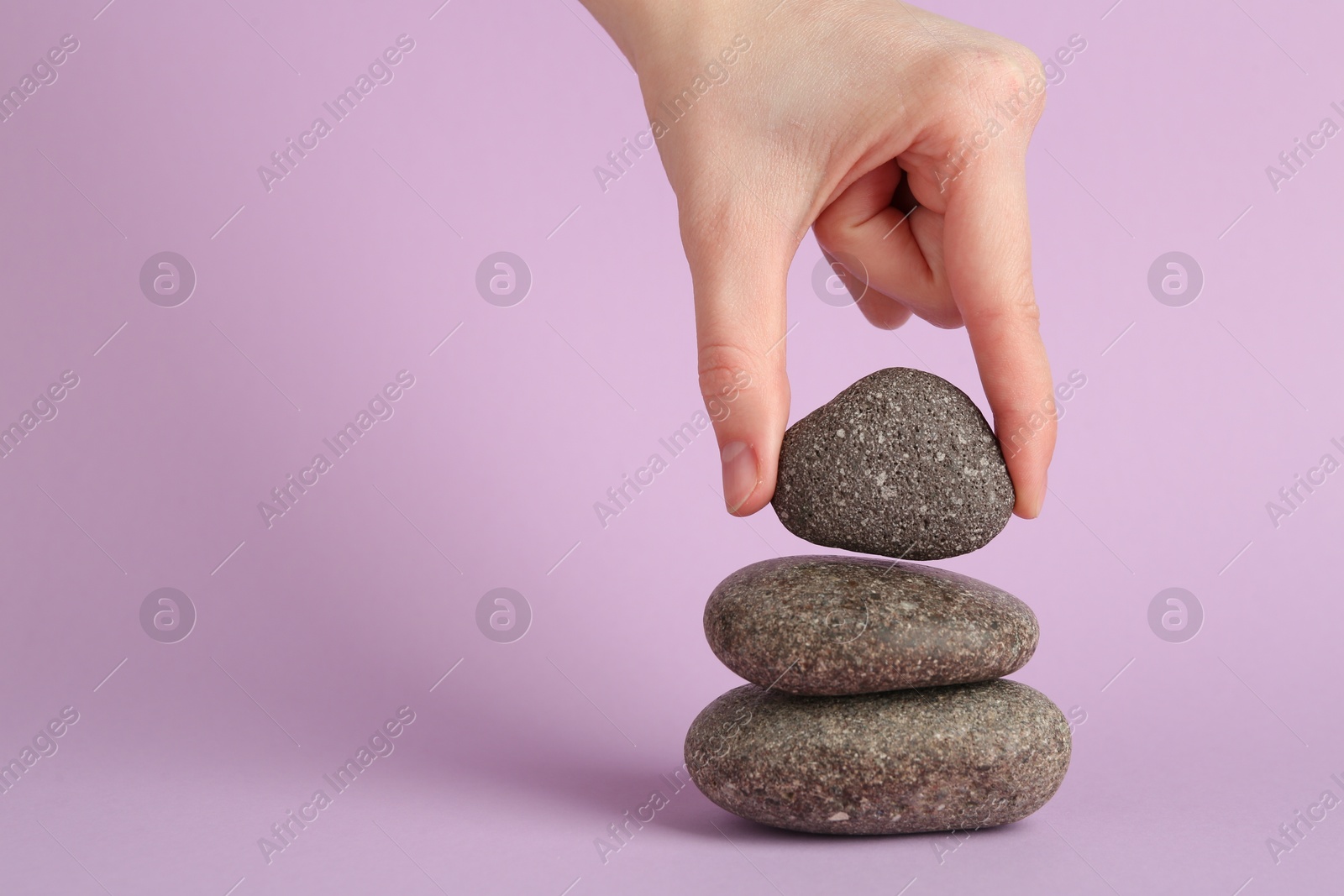 Photo of Woman making stack of stones on lilac background, closeup with space for text. Harmony and life balance