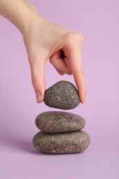 Photo of Woman making stack of stones on lilac background, closeup. Harmony and life balance