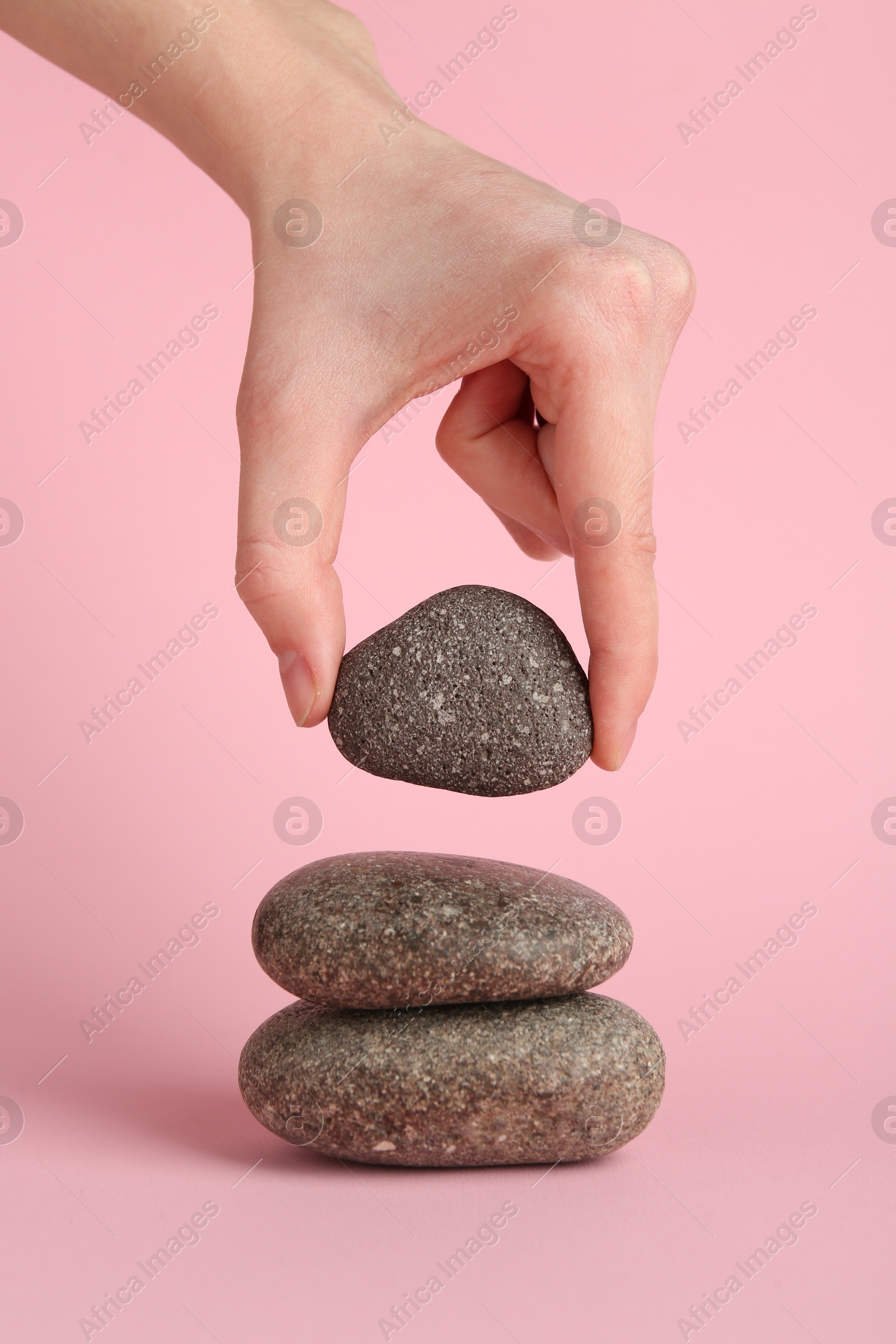 Photo of Woman making stack of stones on light pink background, closeup. Harmony and life balance