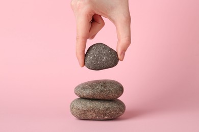 Photo of Woman making stack of stones on light pink background, closeup. Harmony and life balance