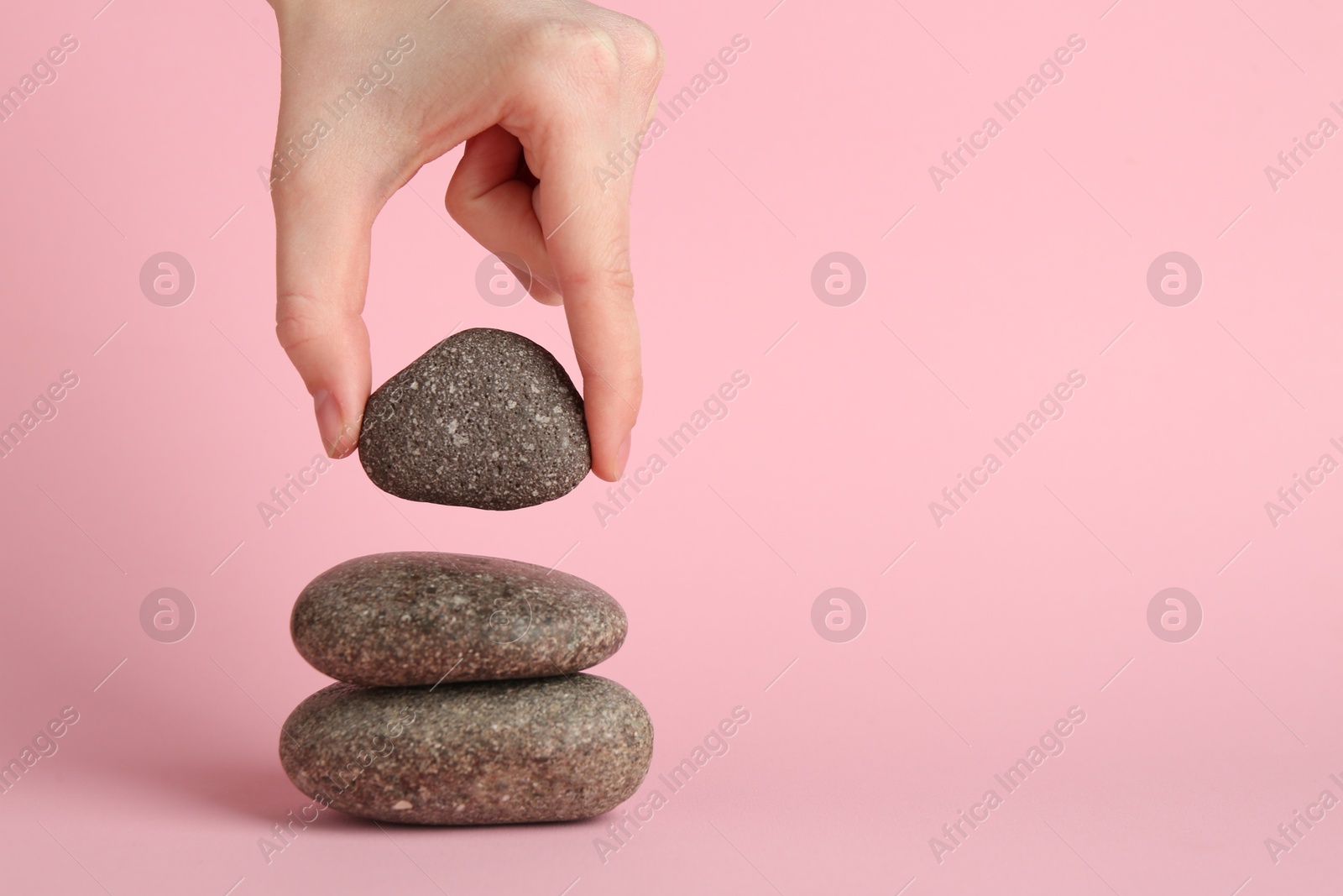 Photo of Woman making stack of stones on light pink background, closeup. Harmony and life balance