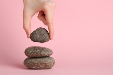 Photo of Woman making stack of stones on light pink background, closeup. Harmony and life balance