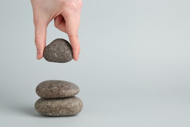 Photo of Woman making stack of stones on light grey background, closeup with space for text. Harmony and life balance