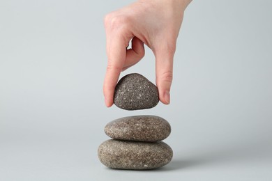 Photo of Woman making stack of stones on light grey background, closeup. Harmony and life balance