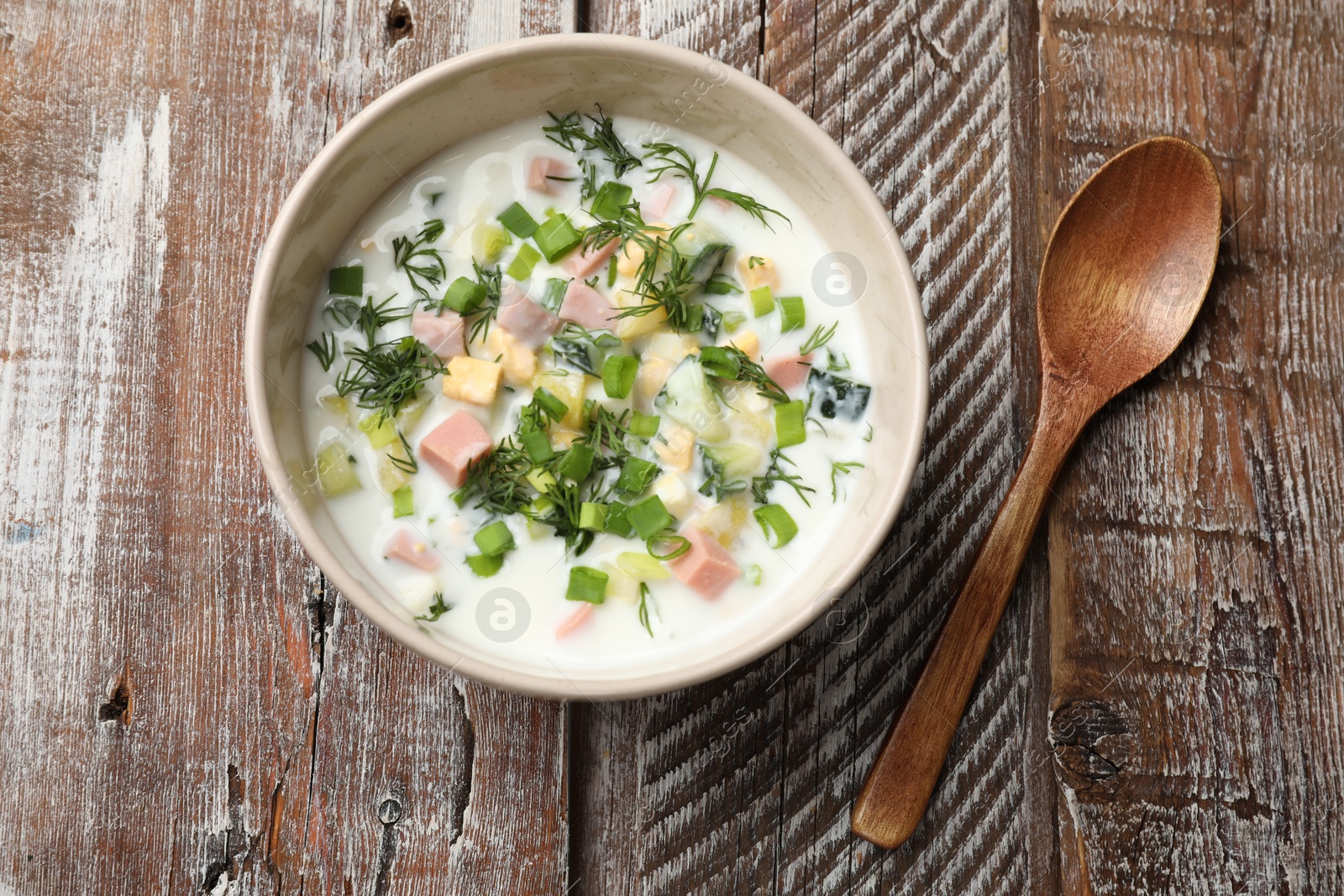 Photo of Delicious okroshka soup in bowl and spoon on wooden table, top view