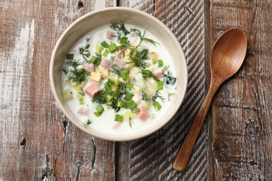 Photo of Delicious okroshka soup in bowl and spoon on wooden table, top view