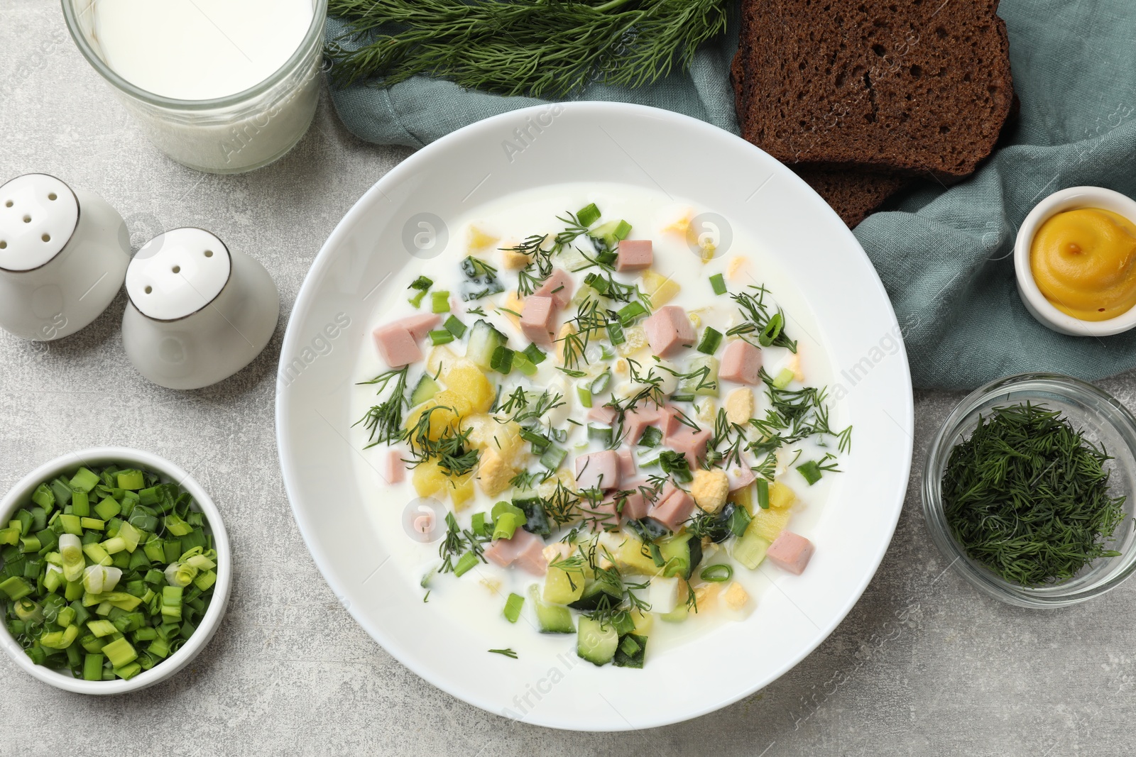 Photo of Delicious okroshka soup in bowl, herbs, bread and spices on grey textured table, flat lay