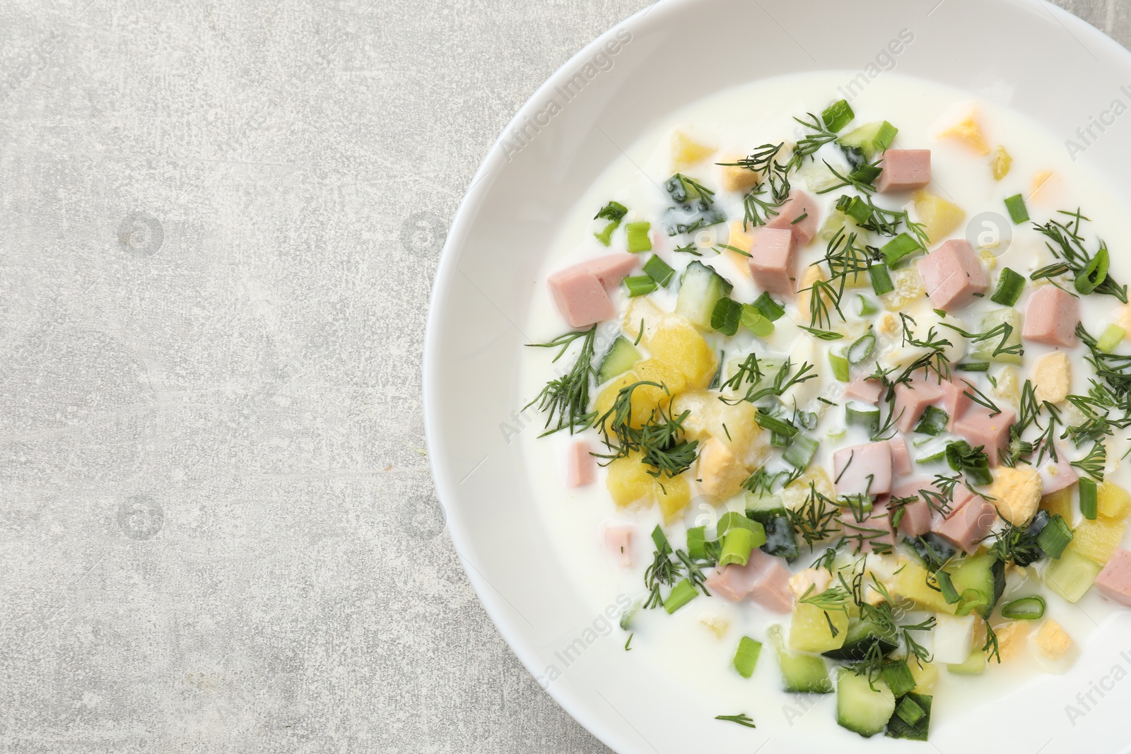 Photo of Delicious okroshka soup in bowl on grey textured table, top view. Space for text