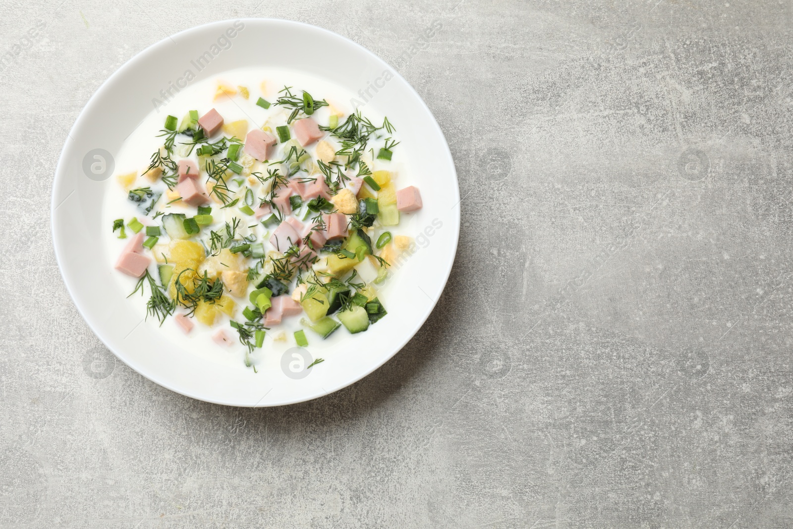 Photo of Delicious okroshka soup in bowl on grey textured table, top view. Space for text