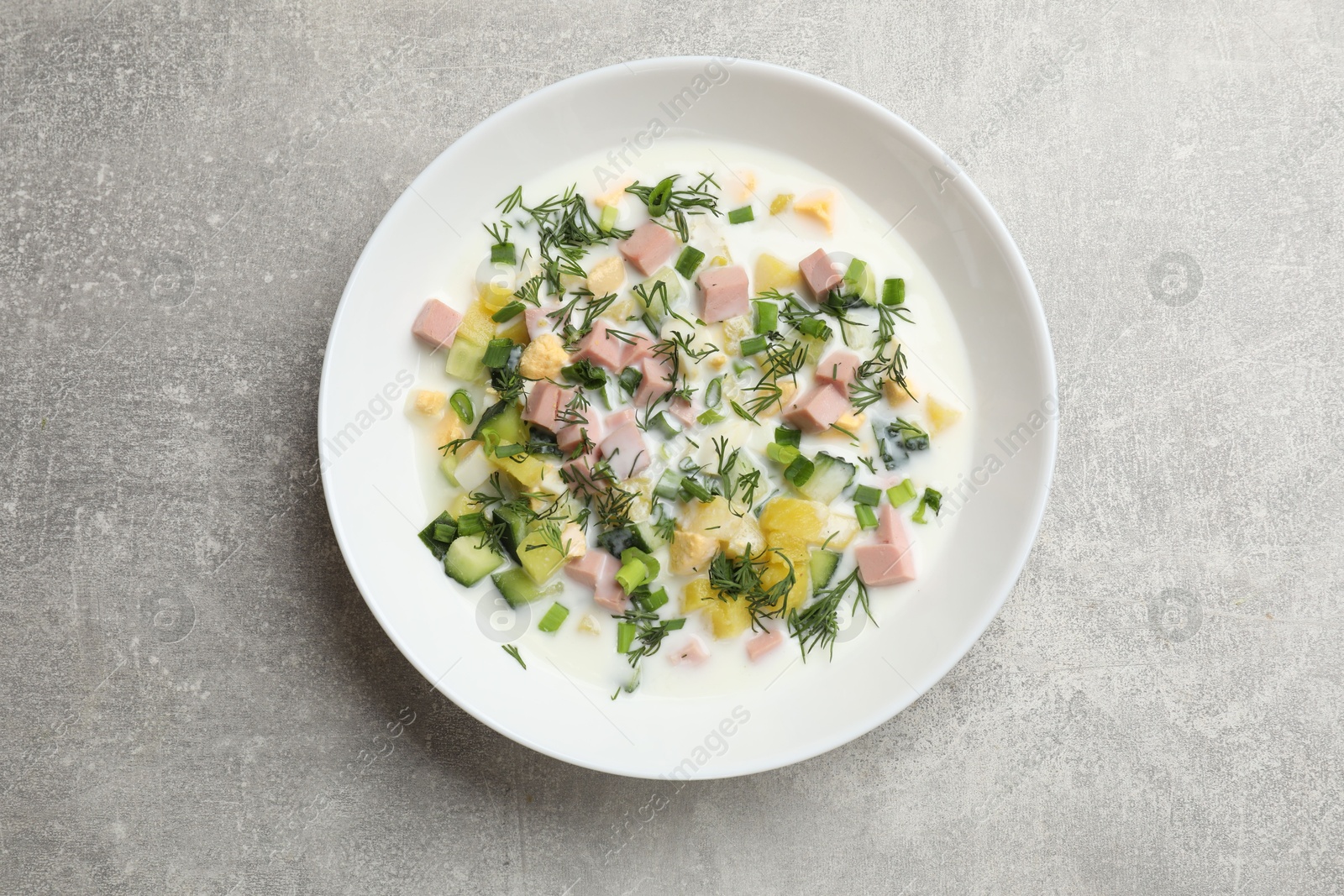 Photo of Delicious okroshka soup in bowl on grey textured table, top view