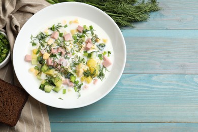 Delicious okroshka soup in bowl on light blue wooden table, flat lay. Space for text