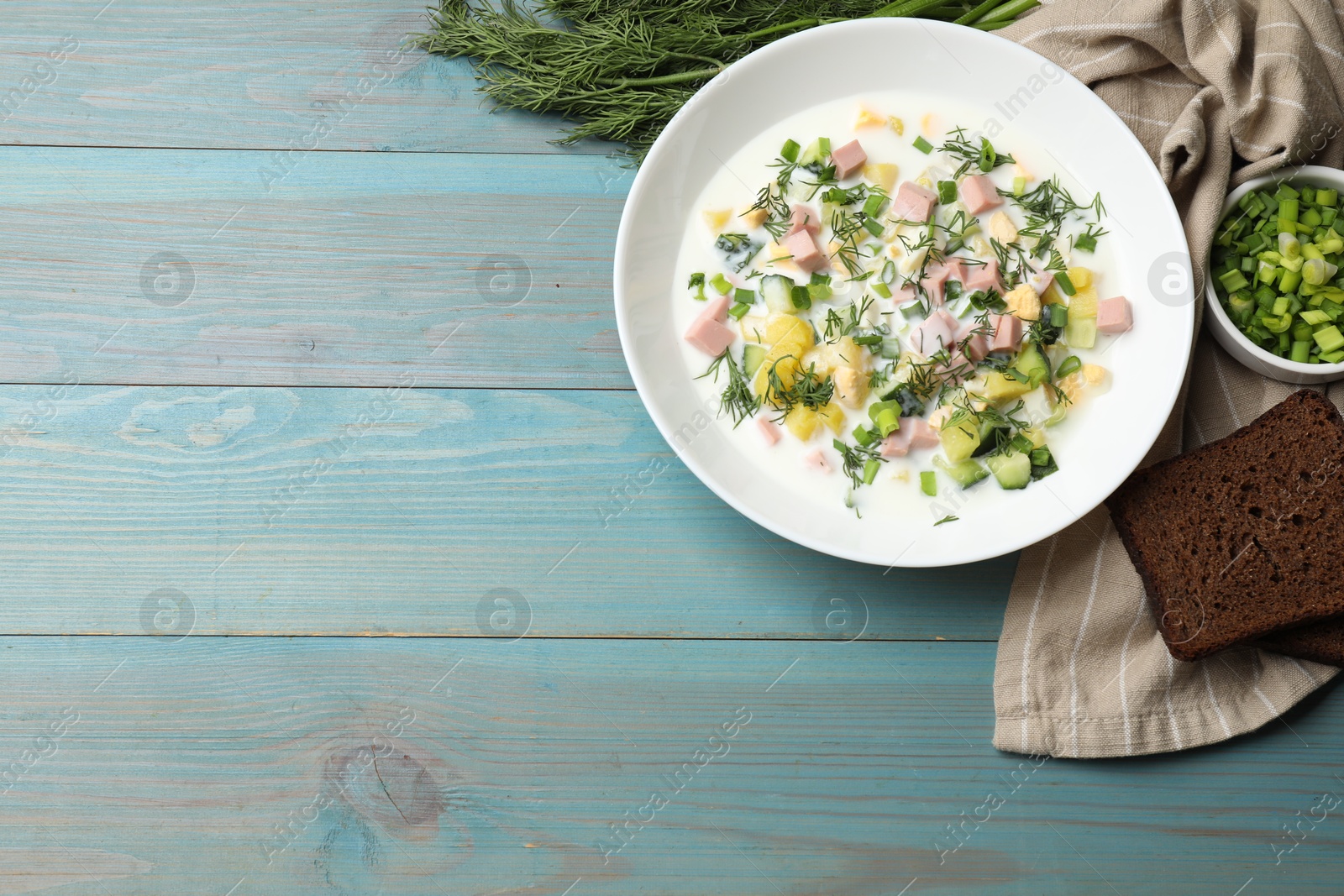 Photo of Delicious okroshka soup in bowl on light blue wooden table, flat lay. Space for text