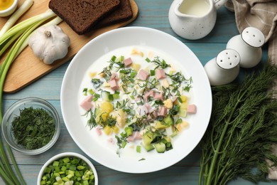 Photo of Delicious okroshka soup in bowl and products on light blue wooden table, flat lay