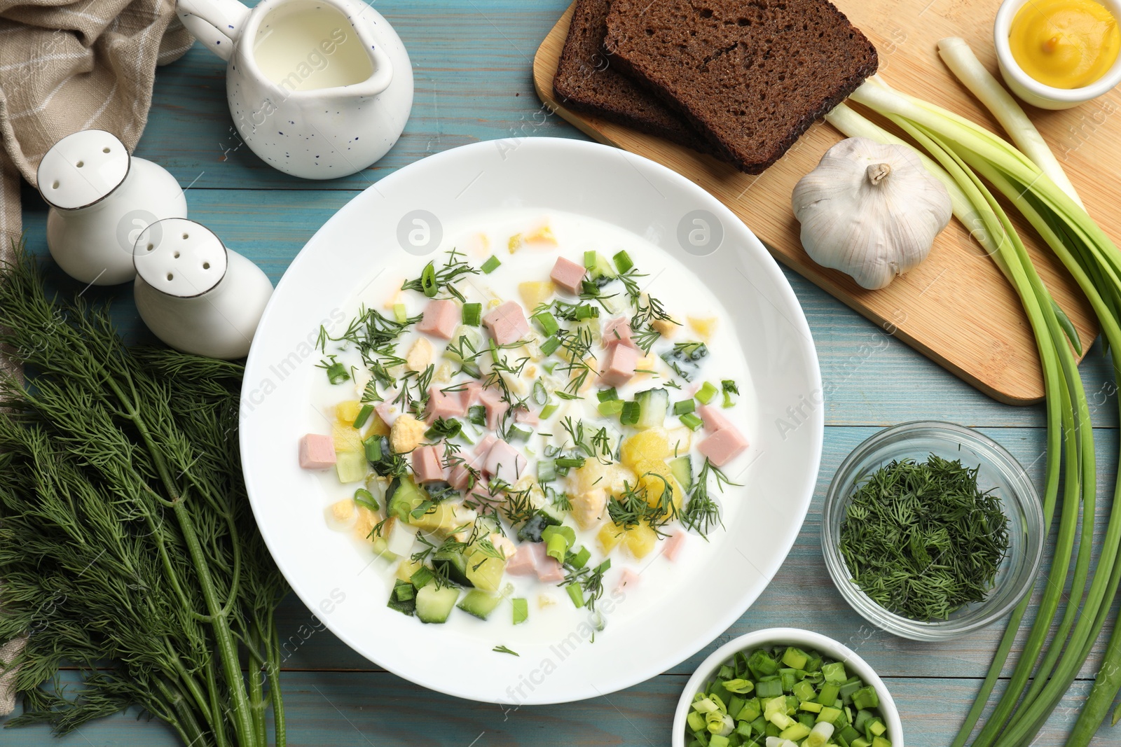 Photo of Delicious okroshka soup in bowl and products on light blue wooden table, flat lay