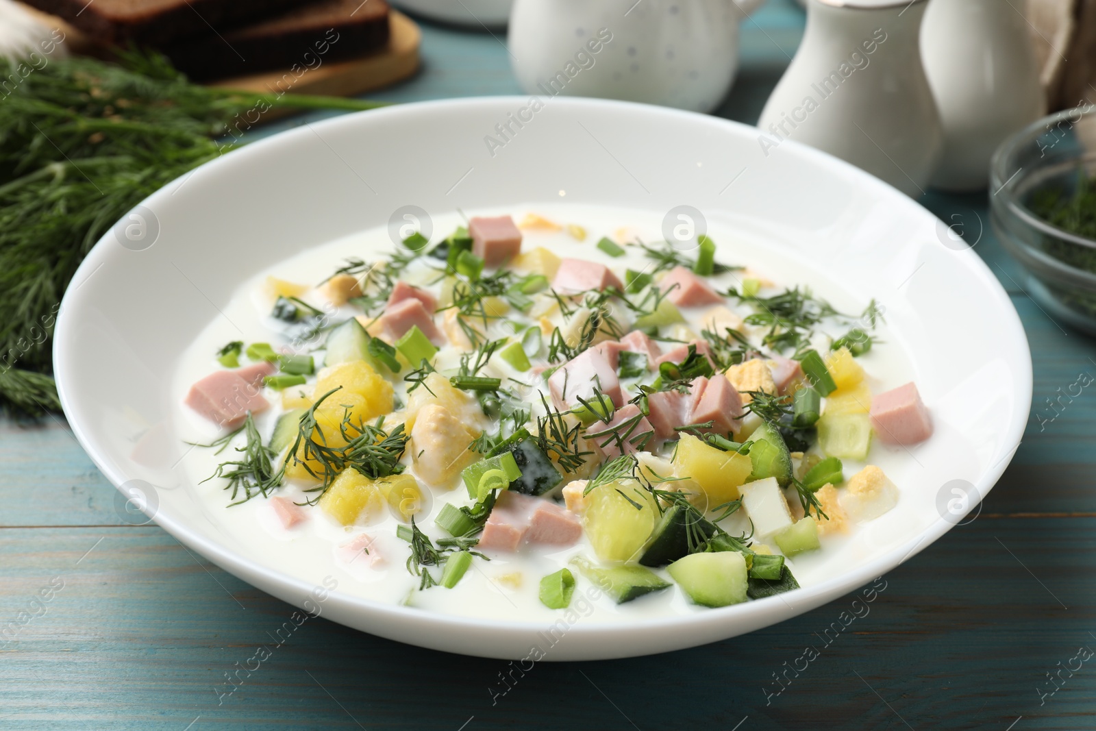 Photo of Delicious okroshka soup in bowl on light blue wooden table, closeup