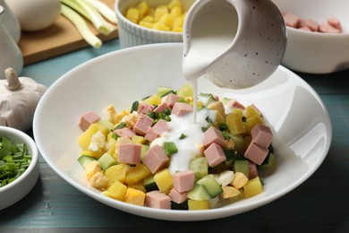 Photo of Making okroshka soup. Pouring kefir into bowl with different ingredients at light blue wooden table, closeup