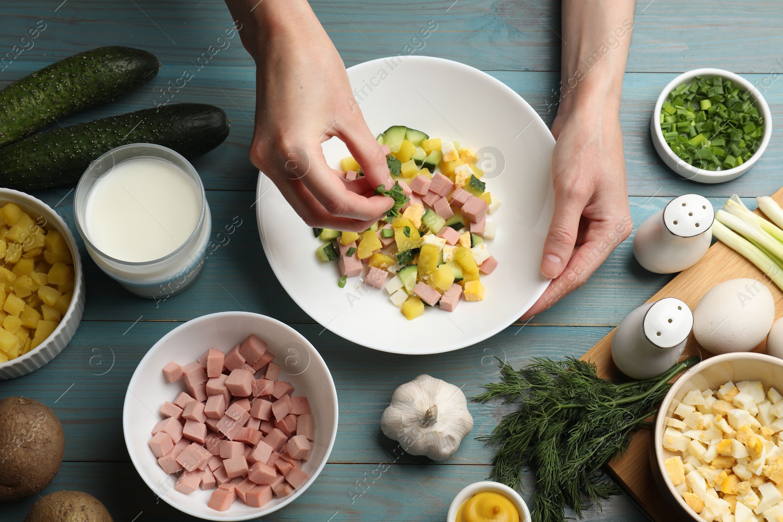 Photo of Woman adding green onion into bowl with okroshka soup at light blue wooden table, top view