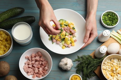 Photo of Woman adding green onion into bowl with okroshka soup at light blue wooden table, top view