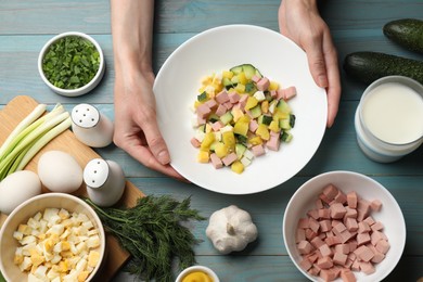 Photo of Woman with ingredients for okroshka soup at light blue wooden table, top view