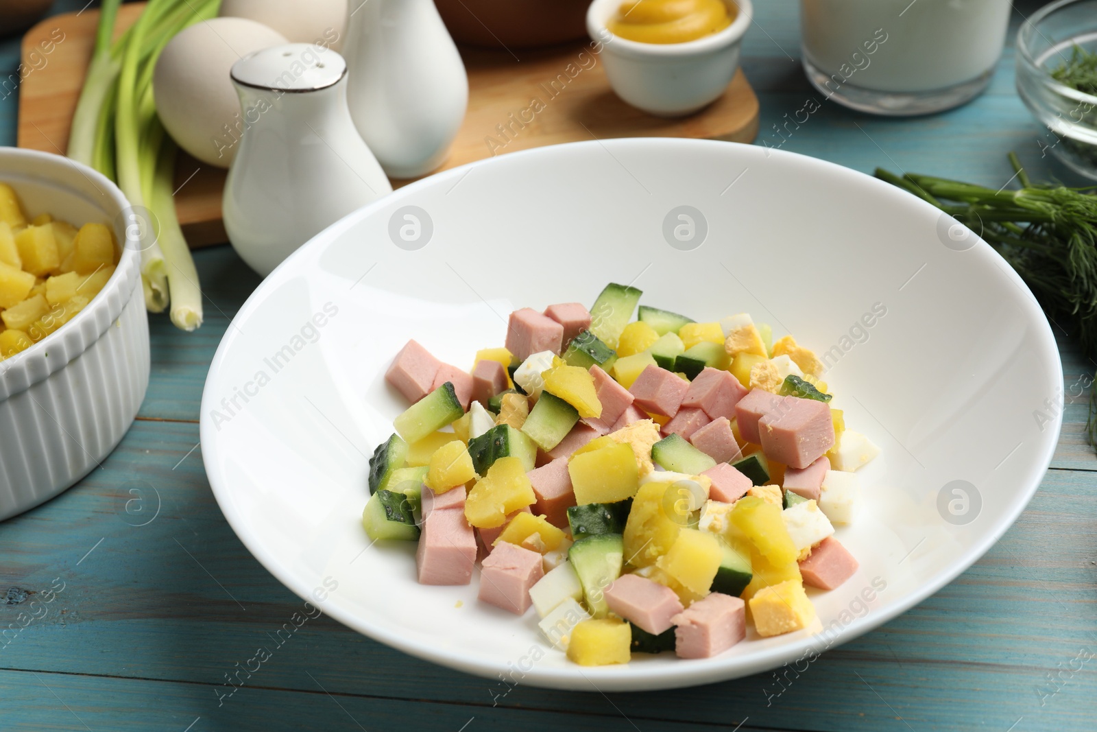 Photo of Ingredients for okroshka soup in bowl on light blue wooden table, closeup