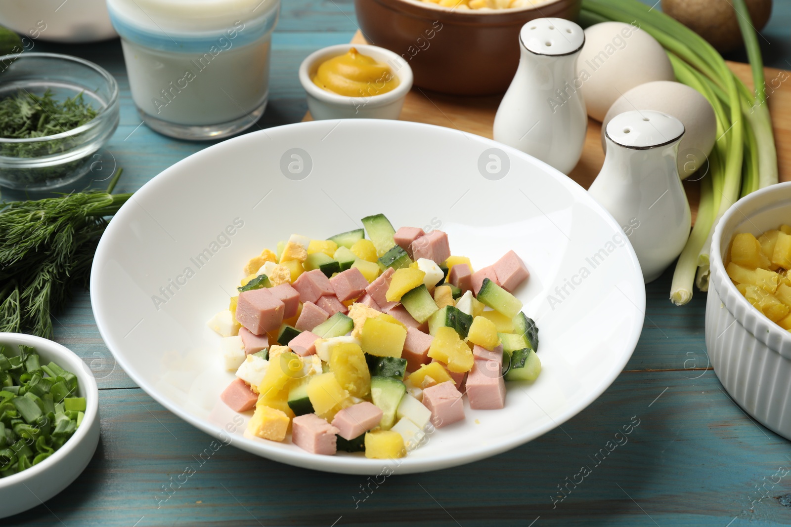 Photo of Ingredients for okroshka soup in bowl on light blue wooden table, closeup