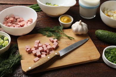 Photo of Cut ingredients for okroshka soup and knife on wooden table, closeup