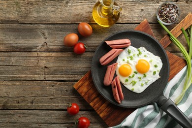 Photo of Tasty fried eggs with cut sausages served on wooden table, flat lay. Space for text