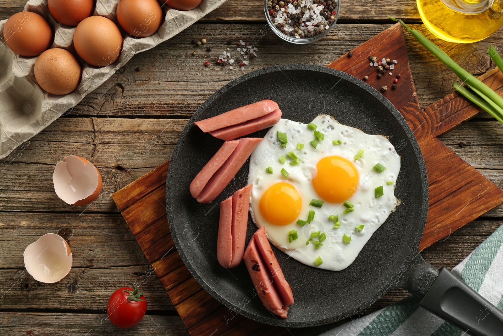 Photo of Tasty fried eggs with cut sausages served on wooden table, flat lay