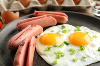 Photo of Tasty fried eggs with cut sausages and green onion in frying pan on table, closeup