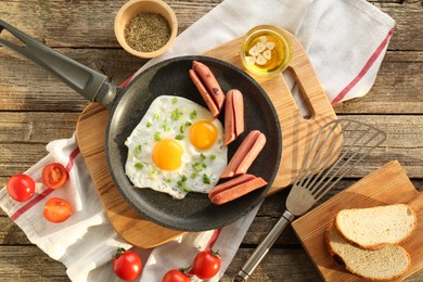 Photo of Tasty fried eggs with cut sausages served on wooden table, flat lay