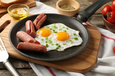 Photo of Tasty fried eggs with cut sausages served on wooden table, closeup