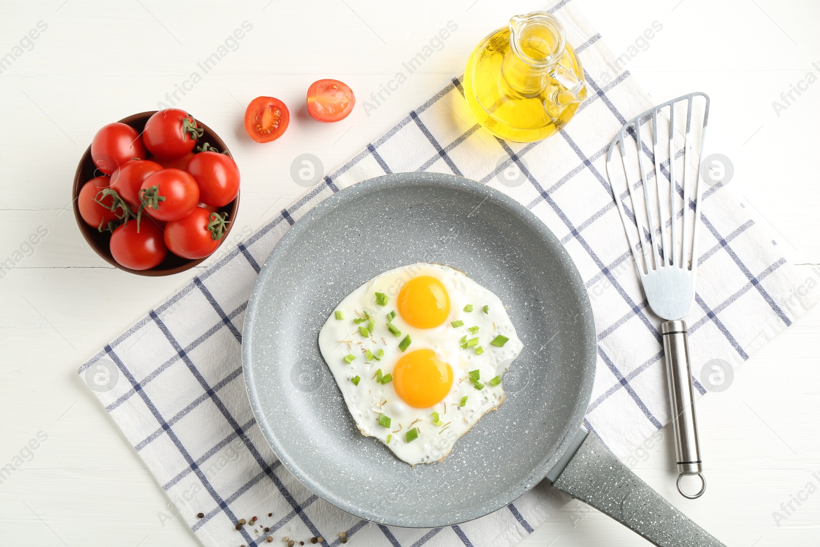 Photo of Tasty fried eggs with green onion in frying pan, oil and tomatoes on white wooden table, flat lay