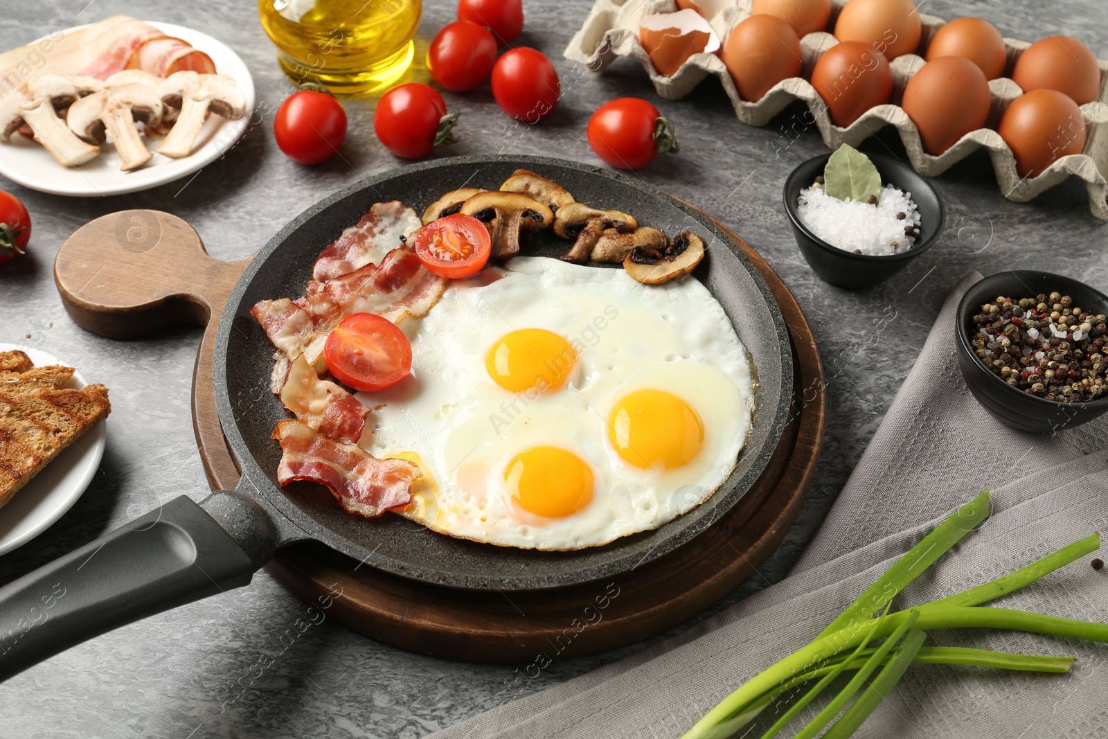 Photo of Tasty fried eggs with bacon and mushrooms served on grey table