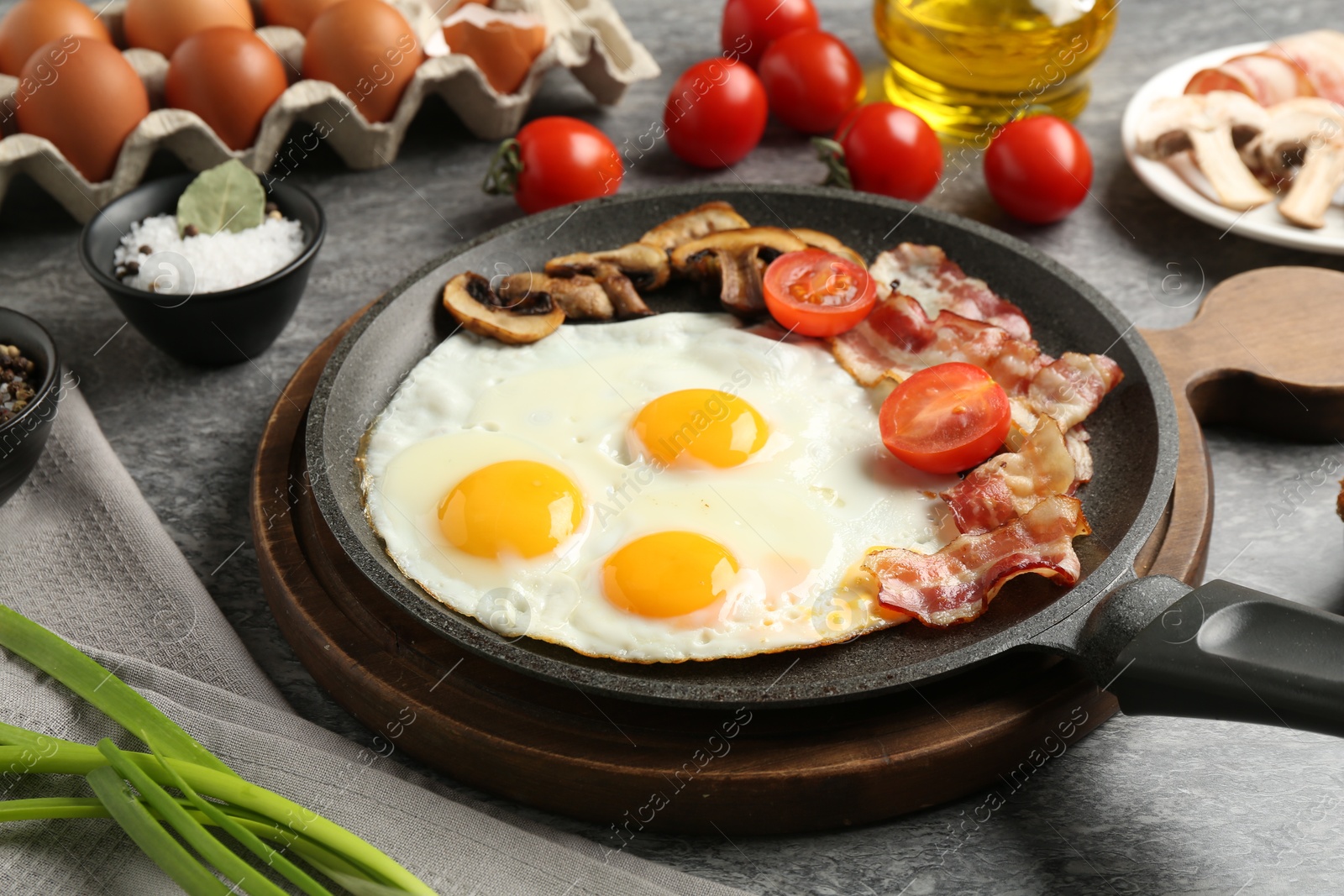 Photo of Tasty fried eggs with bacon and mushrooms served on grey table, closeup