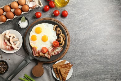 Photo of Tasty fried eggs with bacon and mushrooms served on grey table, flat lay. Space for text