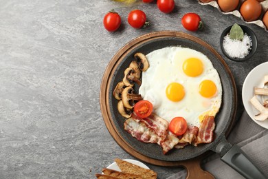 Photo of Tasty fried eggs with bacon and mushrooms served on grey table, flat lay. Space for text