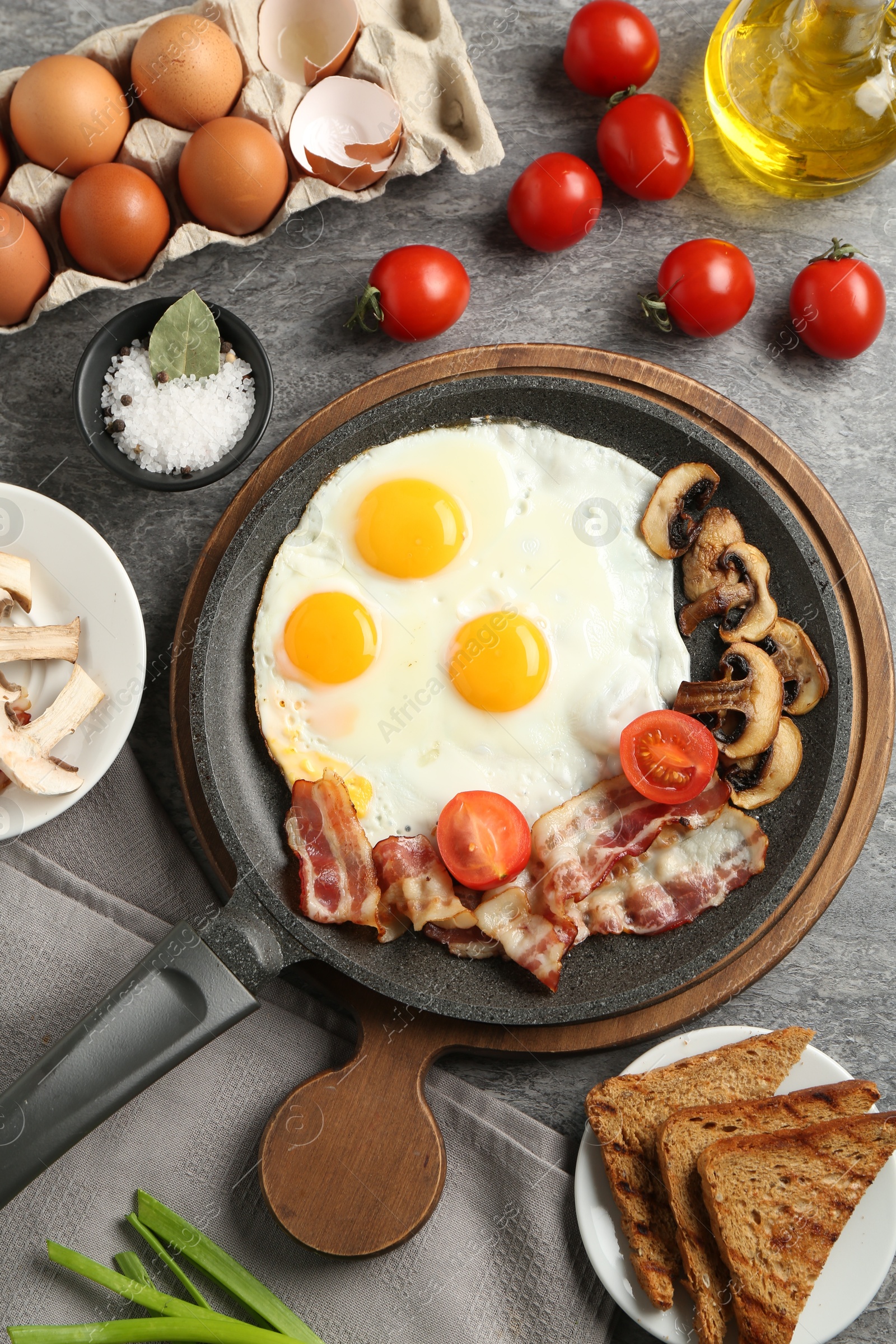 Photo of Tasty fried eggs with bacon and mushrooms served on grey table, flat lay