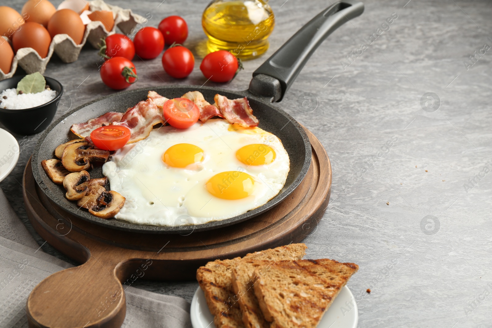 Photo of Tasty fried eggs with bacon and mushrooms served on grey table, closeup. Space for text