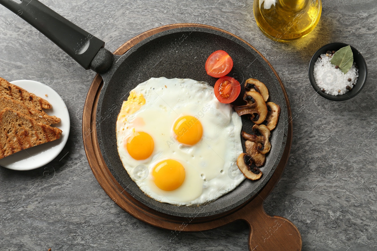 Photo of Tasty fried eggs with mushrooms served on grey table, flat lay