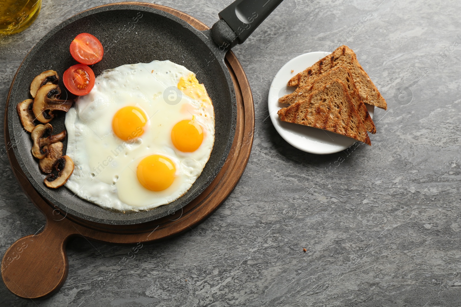 Photo of Tasty fried eggs with mushrooms served on grey table, flat lay