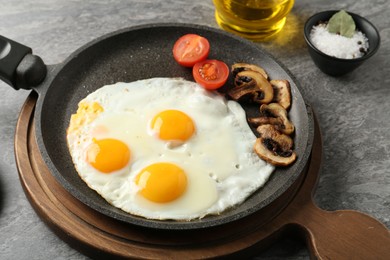 Photo of Tasty fried eggs with mushrooms served on grey table, closeup