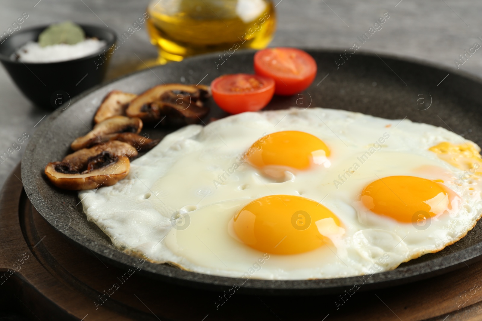 Photo of Tasty fried eggs with mushrooms and tomato in frying pan on table, closeup