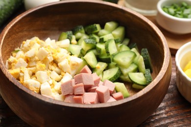 Photo of Different ingredients for okroshka soup in bowl on wooden table, closeup