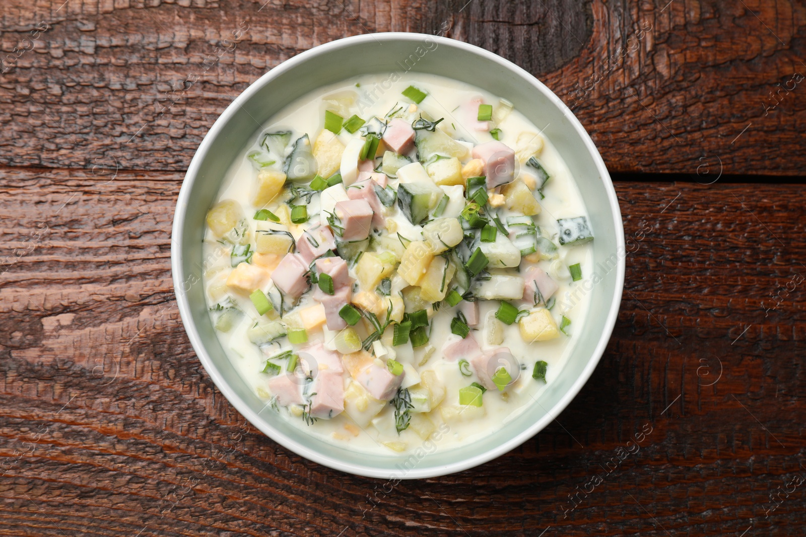 Photo of Delicious okroshka soup in bowl on wooden table, top view