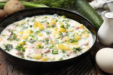 Photo of Delicious okroshka soup with kefir in bowl and ingredients on wooden table, closeup